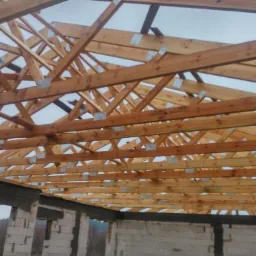 Konstrukcja drewniana dachu z widocznymi metalowymi łącznikami w trakcie budowy domu z białego bloczka.