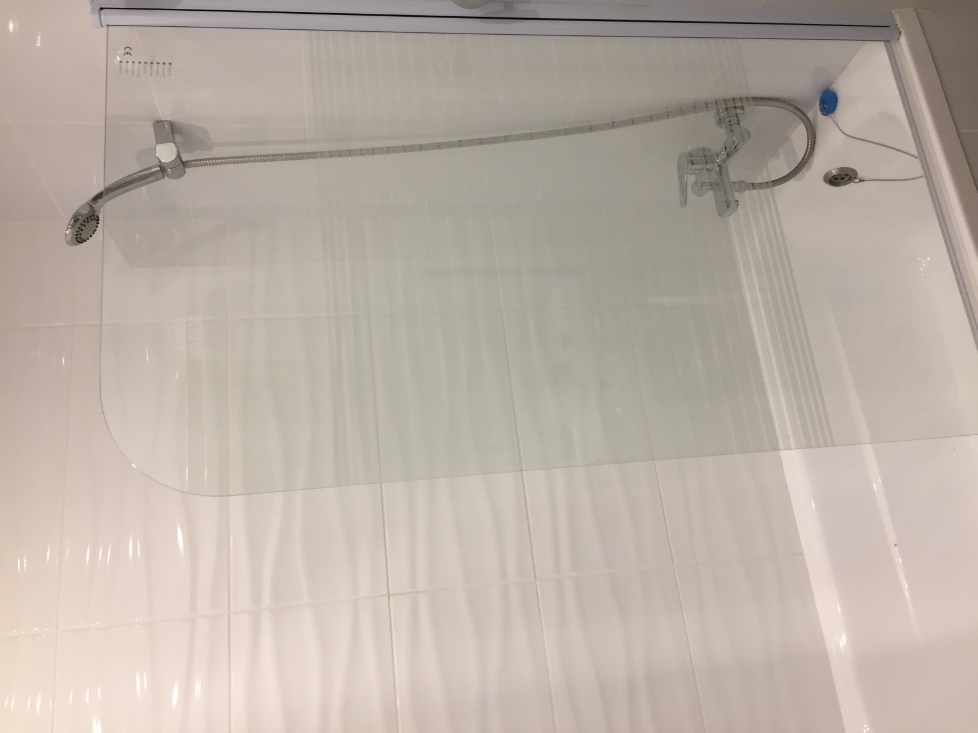 Szklana kabina prysznicowa z chromowaną armaturą i białymi, falistymi płytkami ściennymi w minimalistycznej łazience.