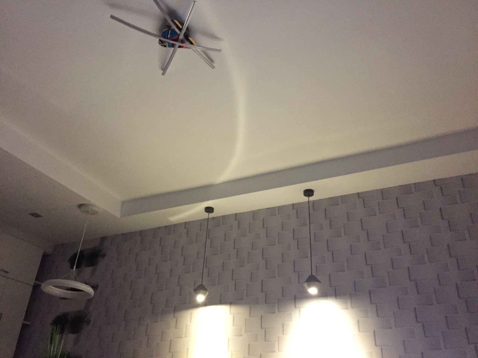 Nowoczesne oświetlenie sufitowe z dekoracyjną lampą w kształcie kuli z wystającymi prętami oraz dwie wiszące lampy z małymi kloszami na tle ściany z trójwymiarową teksturą cegieł.