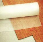 Rolka białej folii ochronnej na panelach podłogowych, widok z góry, delikatne światło, faktura drewna, częściowe rozwinięcie, zabezpieczenie podłogi.