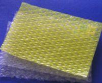 Dwa arkusze folii bąbelkowej: żółty na wierzchu i przezroczysty pod spodem. Widoczna struktura bąbelków, lekko nieostre tło.