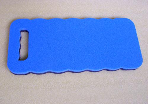 Niebieska, prostokątna mata piankowa z uchwytem i falistym brzegiem na beżowym tle. Idealna jako podkładka ochronna lub do klękania podczas prac.