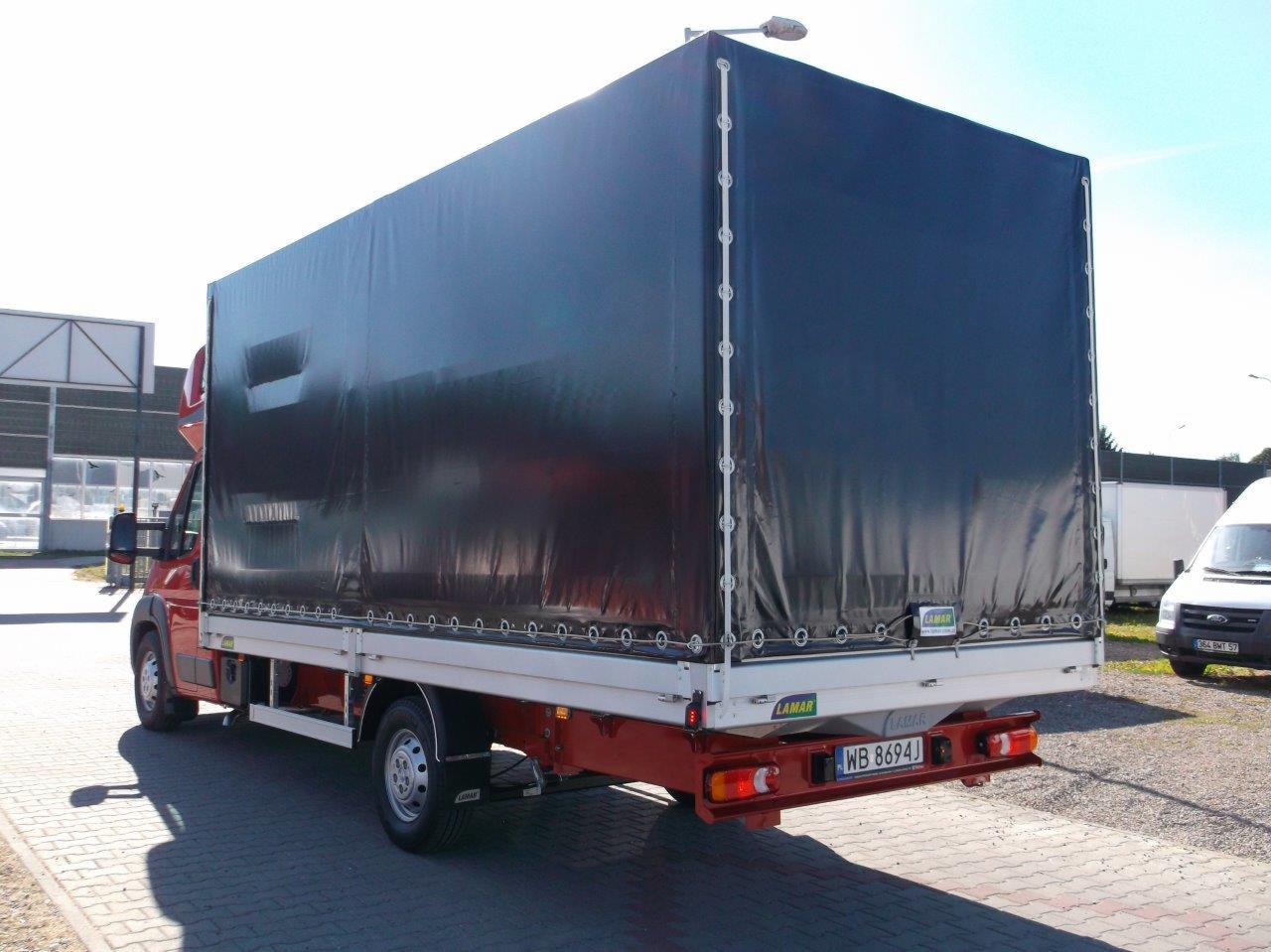 Czerwony samochód dostawczy Peugeot Boxer z plandeką, widok z tyłu, tablica rejestracyjna WB 8694J, na parkingu.