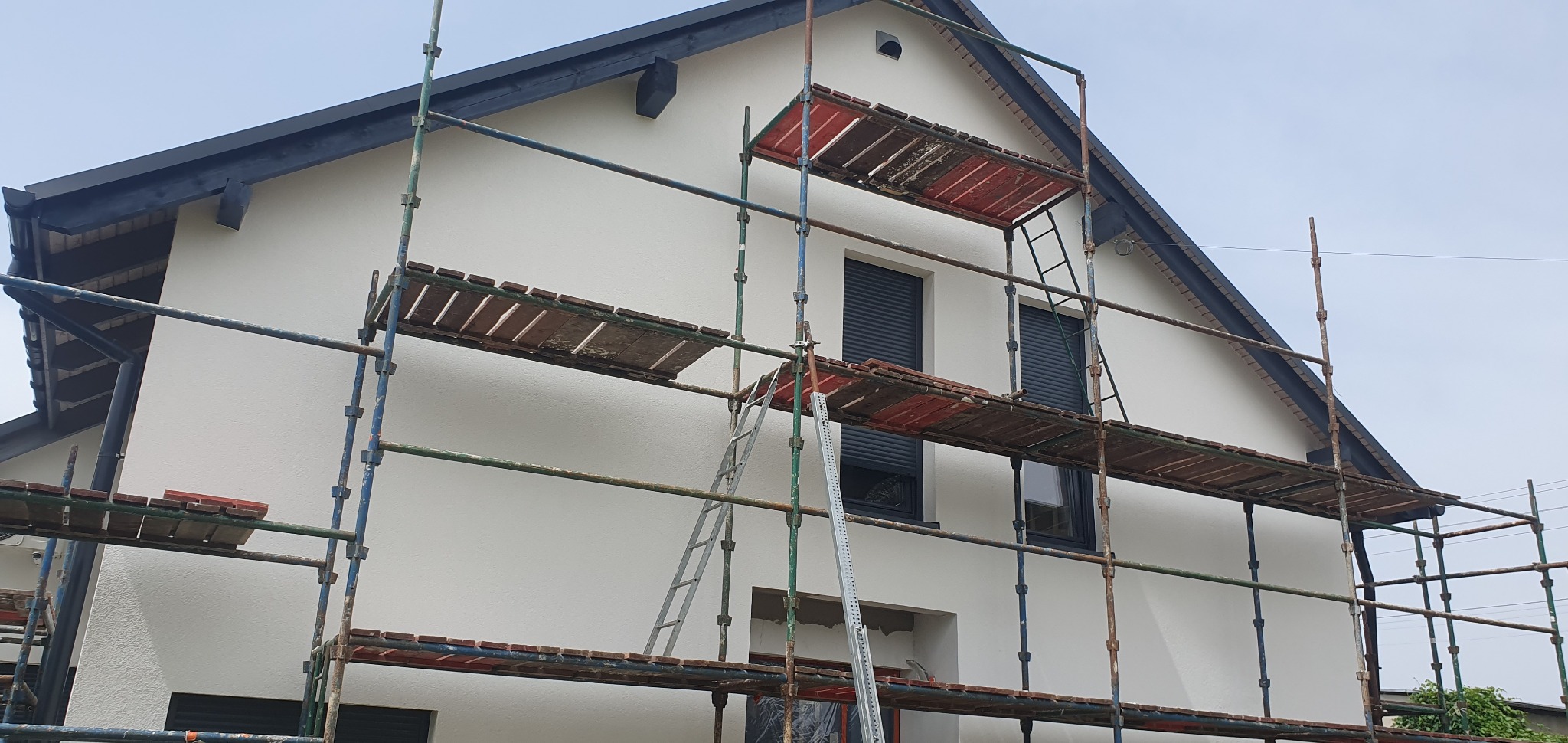 Elewacja domu jednorodzinnego w Rusinowicach po remoncie, z rusztowaniem. Świeżo pomalowana, biała fasada, czarne okna i dach. Widoczne detale wykończenia.