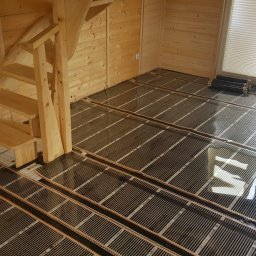 STELKAM.pl - Instalacja mat grzewczych w drewnianym domu w Górowie Iławeckim, widoczne etapy układania pod system ogrzewania podłogowego oraz fragment drewnianych schodów.