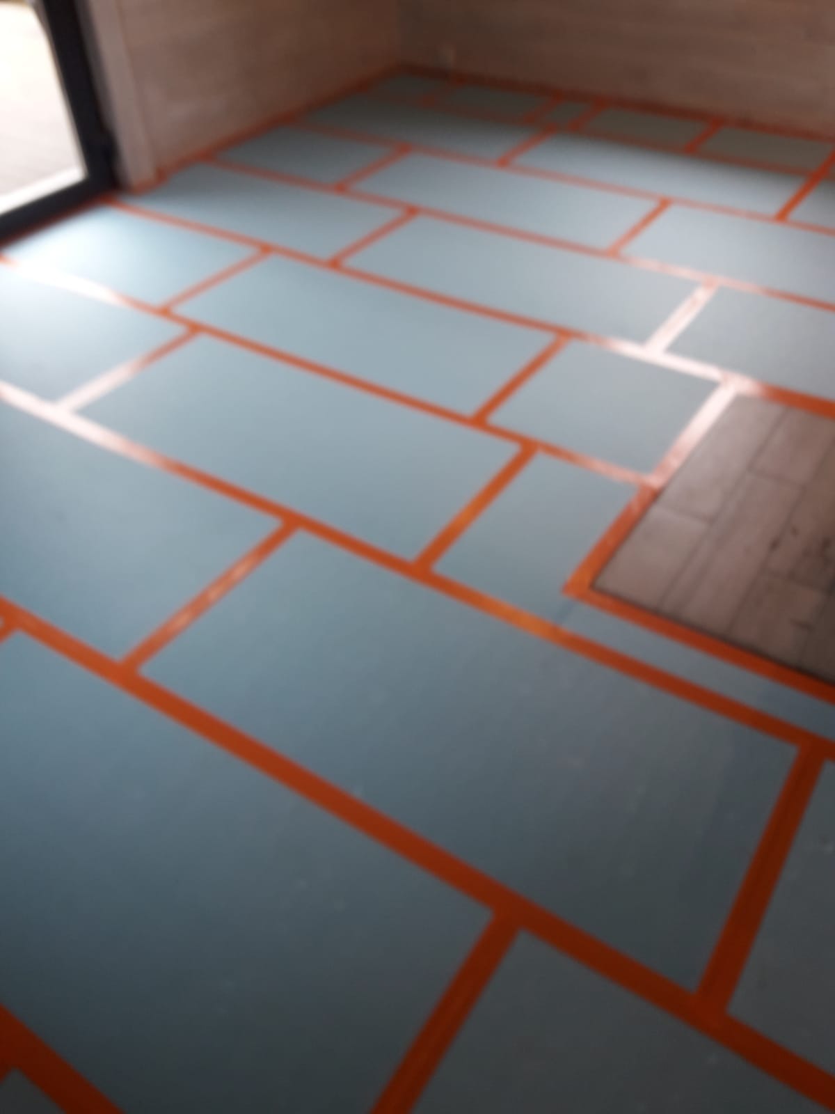 Przygotowanie podłoża pod instalację ogrzewania podłogowego: płyty izolacyjne ułożone na podłodze, wyznaczone pomarańczową taśmą. Widoczne fragmenty starej podłogi.