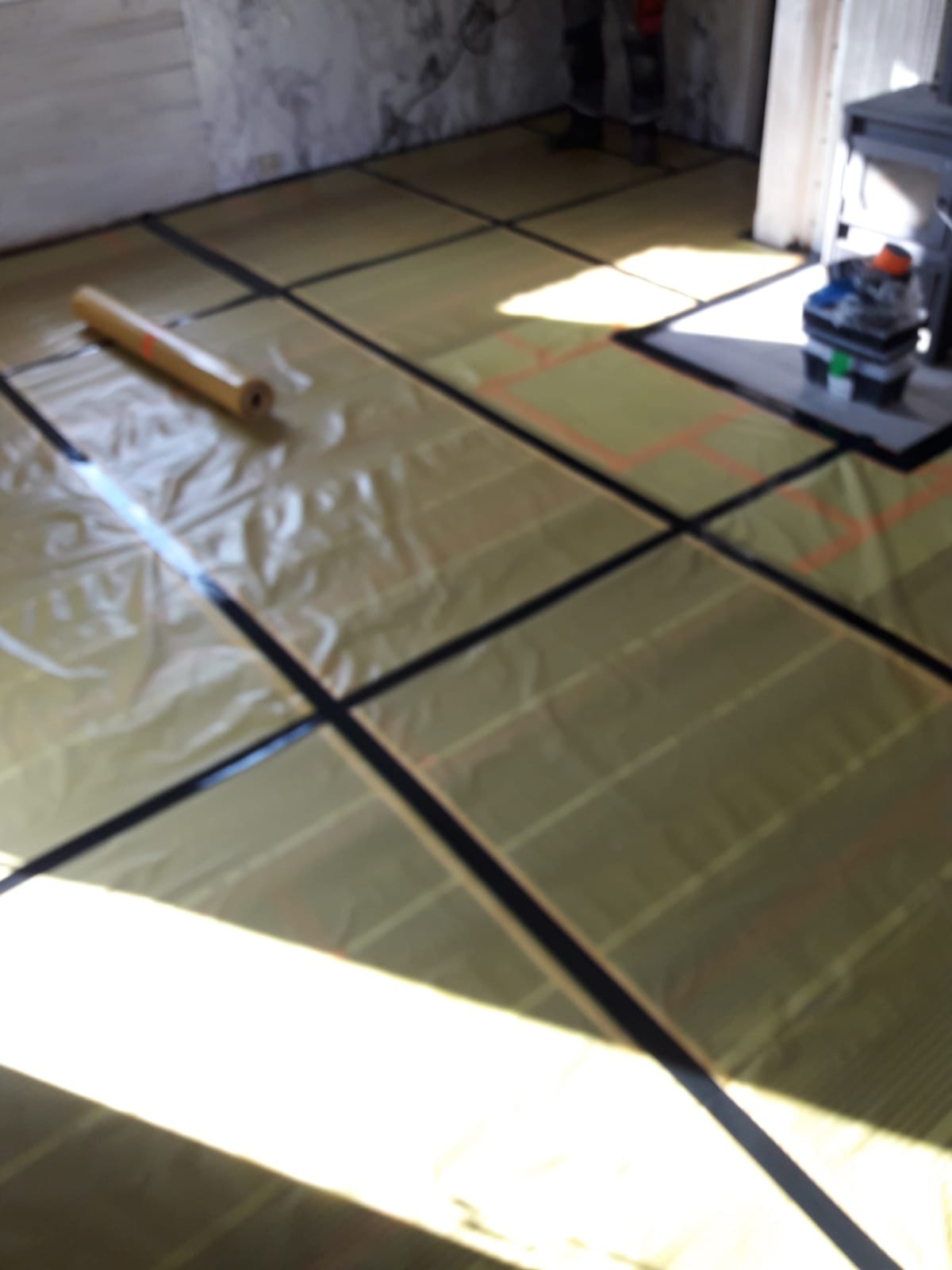 Rozłożona folia grzewcza na podłodze, przygotowana do montażu, widoczny rolka folii i narzędzia w tle.