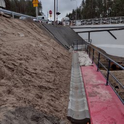 Przedsiębiorstwo Handlowo Usługowe JP Paulina Jastruszewska - Skarpa z betonowymi schodami i korytem odwadniającym. Widoczny fragment mostu i znak drogowy. Prace ziemne w toku, teren przygotowany pod dalsze roboty.