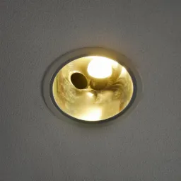 Zamontowana okrągła lampa sufitowa z żarówką, widoczna od dołu na tle białego, chropowatego sufitu. Widoczny otwór obok żarówki.