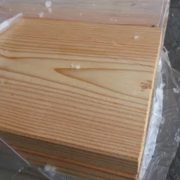 Stos tarcicy budowlanej z widocznym usłojeniem drewna, zabezpieczony folią ochronną.