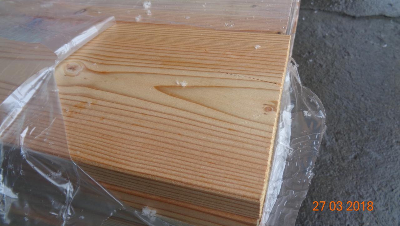 Stos tarcicy budowlanej z widocznym usłojeniem drewna, zabezpieczony folią ochronną.