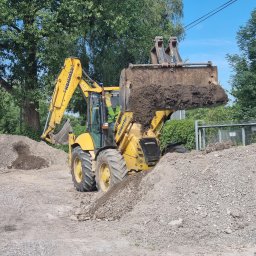 SzkoleniaMM Rafał Dunaj - Żółta koparko-ładowarka Komatsu w trakcie prac ziemnych, nabiera urobek z pryzmy. Operator w kabinie, w tle zieleń drzew i błękitne niebo. Prace ziemne w toku.