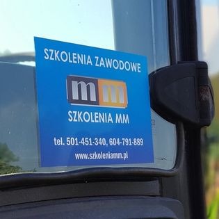 Niebieska naklejka z napisem 'Szkolenia Zawodowe' i logo 'MM Szkolenia MM' umieszczona na szybie pojazdu, widoczne numery telefonów i adres strony internetowej.