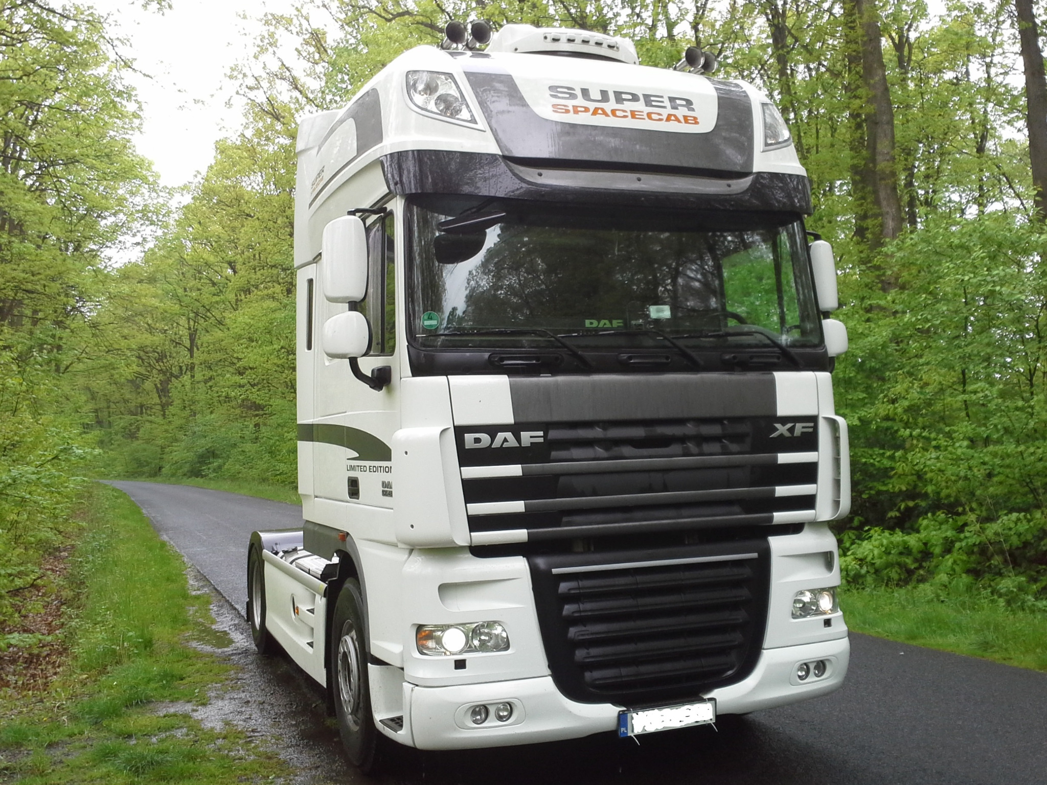 Biała ciężarówka DAF Super Space Cab Limited Edition zaparkowana na asfaltowej drodze w otoczeniu zielonego lasu.