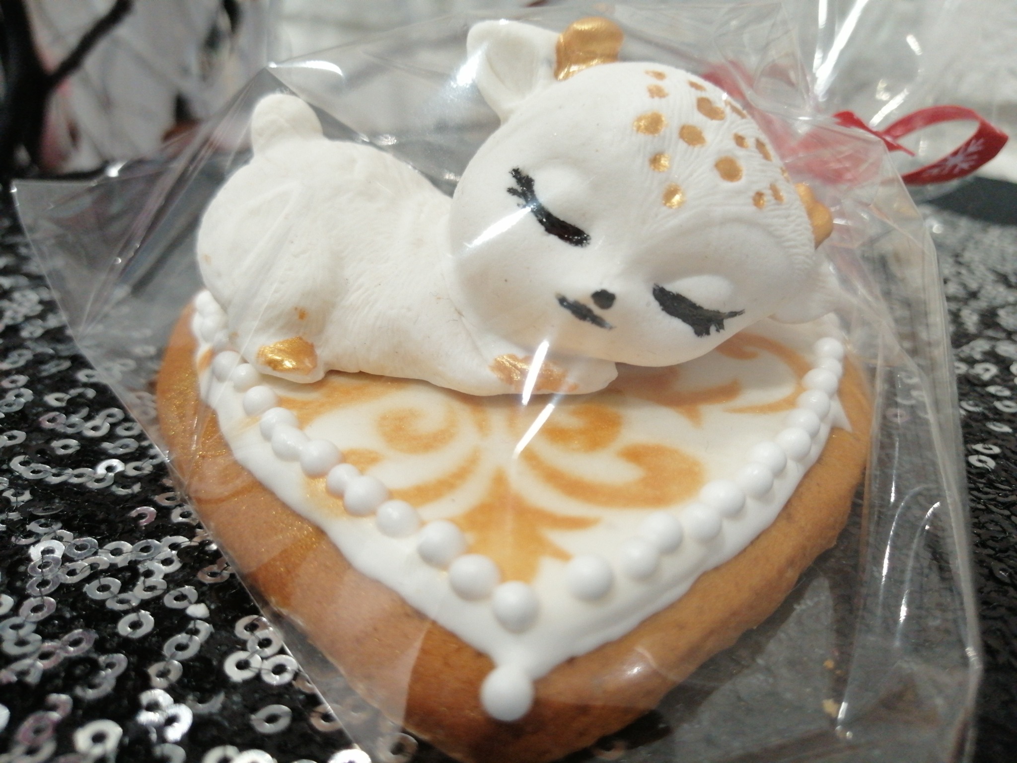 Piernik w kształcie serca z lukrowanym jelonkiem w opakowaniu foliowym z czerwoną wstążką, dekorowany złotymi detalami.