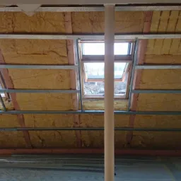 Ocieplenie poddasza wełną mineralną, widoczne okna dachowe i konstrukcja metalowa. Prace wykończeniowe w nowym domu.
