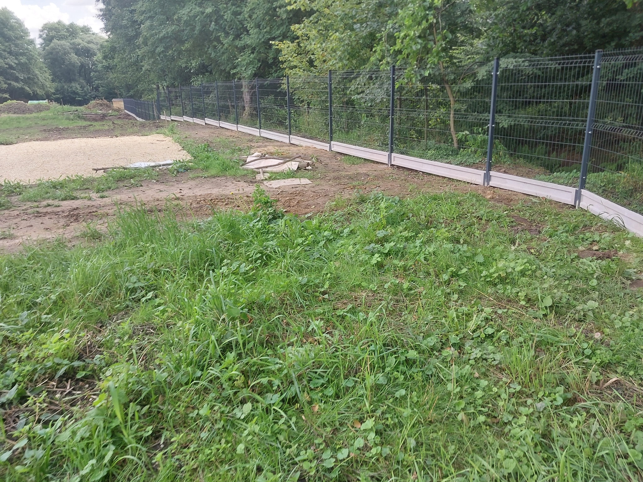 Nowo postawione, ciemne panele ogrodzeniowe na betonowej podmurówce, widoczne na tle zieleni i drzew