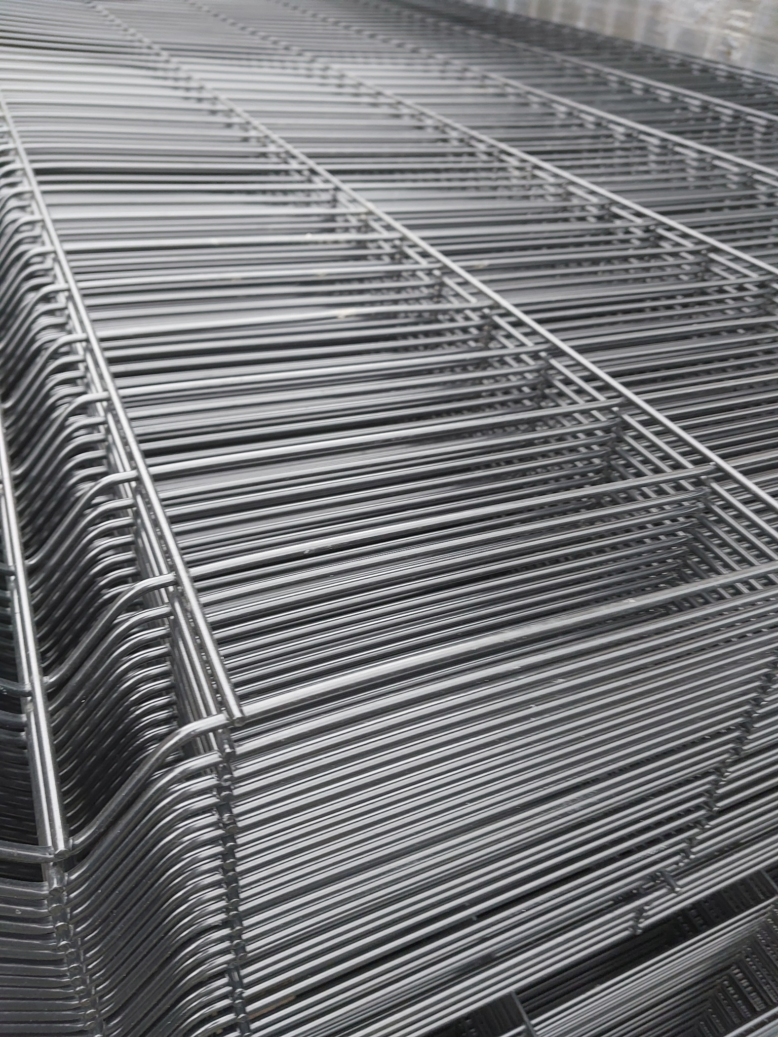 Stos ocynkowanych paneli ogrodzeniowych z drutu, widoczne charakterystyczne zagięcia na krawędziach.