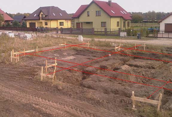 Wytyczone fundamenty pod budowę domu jednorodzinnego na działce z widocznymi sąsiednimi budynkami.