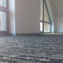 Szara, wzorzysta podłoga z wykładziny dywanowej w jasnym pomieszczeniu z oknami.