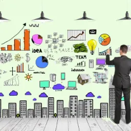 Mężczyzna w garniturze rysuje markerem na ścianie infografiki z wykresami, budynkami i symbolami biznesowymi, oświetlonej przez cztery lampy.