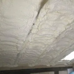 Ocieplenie poddasza pianką PUR z widoczną strukturą piany i fragmentem okna dachowego.