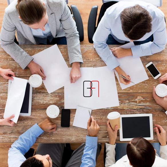 Zespół projektowy omawia logo B&R na kartce papieru leżącej na drewnianym stole, widok z góry, otoczony tabletami, smartfonami, notatnikiem i kawą na wynos.