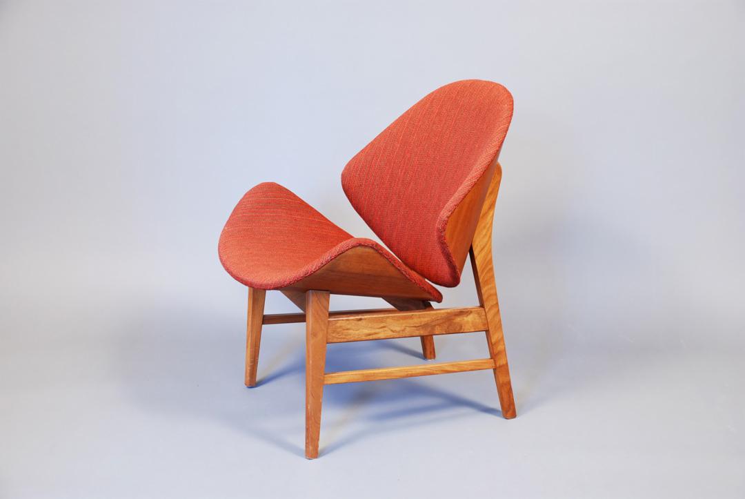 Designerskie krzesło z pomarańczową tapicerką o unikalnym kształcie i drewnianej konstrukcji, sfotografowane na jasnym tle, podkreślające jego nowoczesny styl.