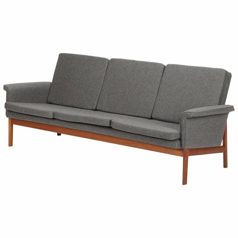 Szara, trzysiedziskowa sofa z drewnianą ramą w stylu skandynawskim, widoczna na białym tle.