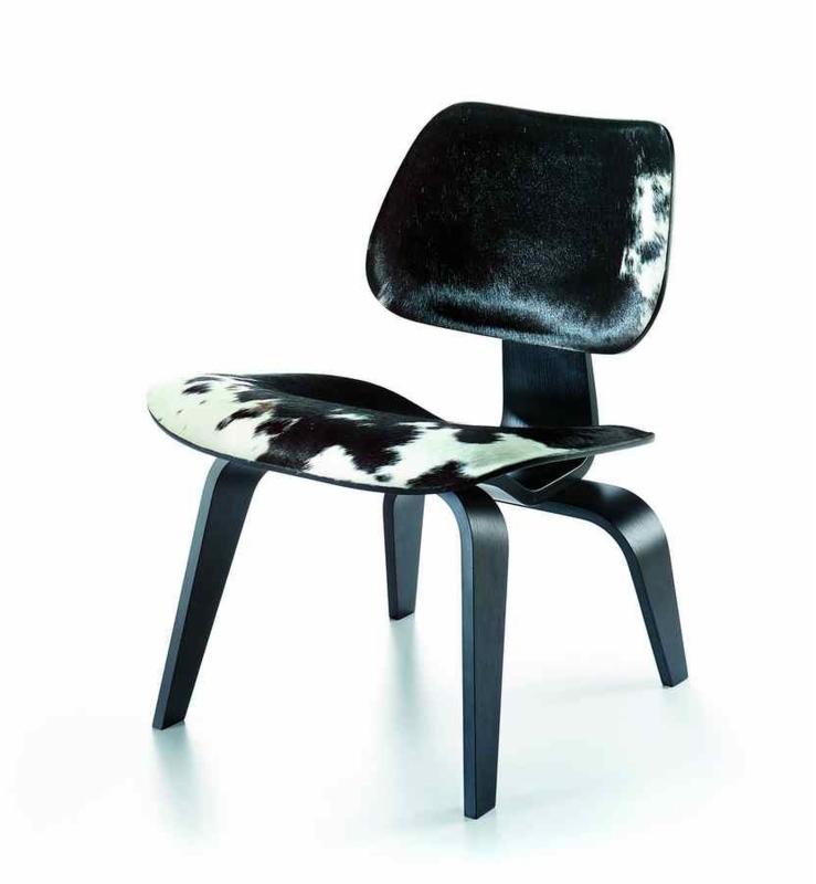Designerskie krzesło z czarnego drewna z siedziskiem i oparciem pokrytym skórą krowy w biało-czarne łaty, na białym tle.