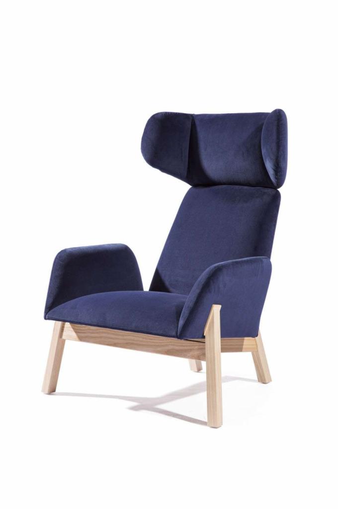 Nowoczesny fotel z wysokim zagłówkiem, obity granatowym welurem, na jasnych drewnianych nogach, sfotografowany w Tychowie na białym tle.