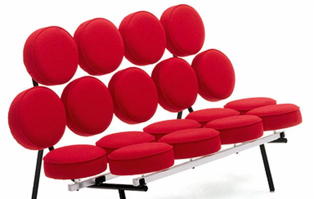 Nowoczesna sofa z czerwonymi, okrągłymi poduszkami na siedzisku i oparciu, wsparta na metalowym stelażu z czarnymi nóżkami, prezentowana na białym tle.