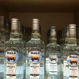 Rzędy butelek wódki Żubrówka Biała, ustawione na półce w hurtowni alkoholi. Widoczne etykiety z wizerunkiem żubra na tle zimowego krajobrazu.