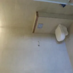 Jasna łazienka z toaletą podwieszaną, oświetleniem LED przy suficie i szarą armaturą, wykończona beżowymi płytkami ceramicznymi.