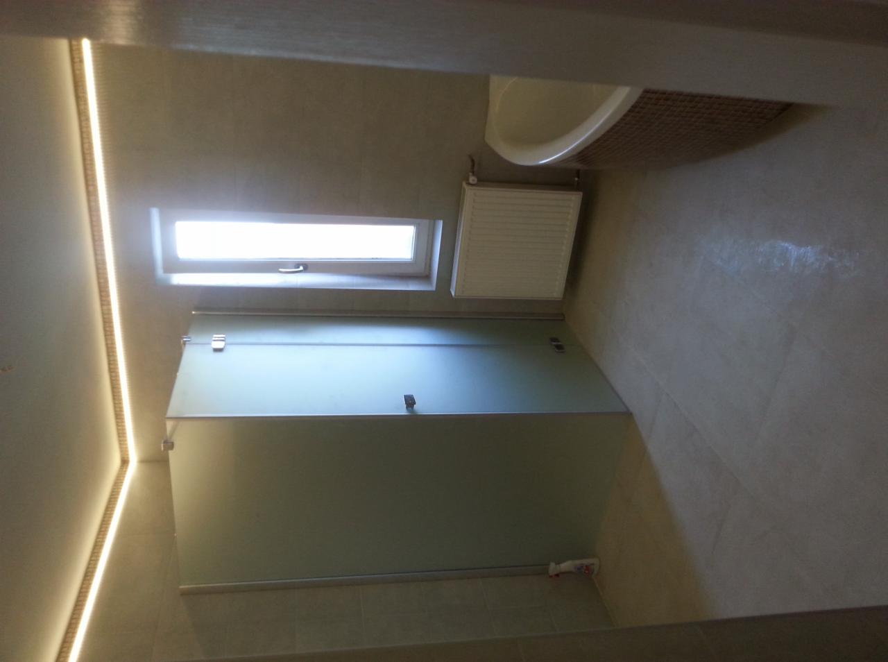 Nowoczesna kabina prysznicowa z matowego szkła w łazience z oknem dachowym i oświetleniem LED podsufitowym.