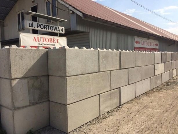 Ułożone prefabrykowane bloczki betonowe na zewnątrz budynku z szyldem 'ul. Portowa 4' i 'AUTOBET Rok Założenia 1993'.