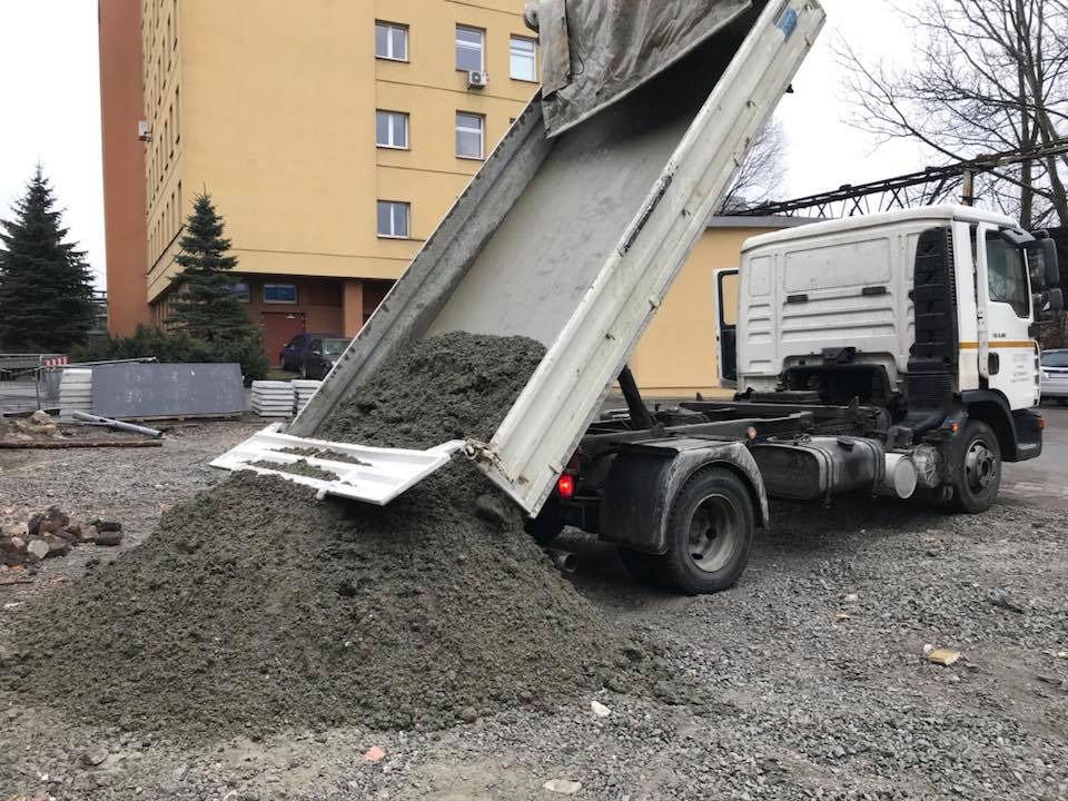 Wyładowywanie betonu z wywrotki na placu budowy, widoczny budynek w tle.