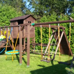 Drewniany plac zabaw z domkiem, zjeżdżalnią i huśtawkami na tle zielonego żywopłotu.