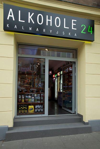 Fasada sklepu z alkoholem z podświetlanym szyldem 'Alkohole Kalwaryjska 24' nad wejściem, widoczne butelki i lodówki wewnątrz.