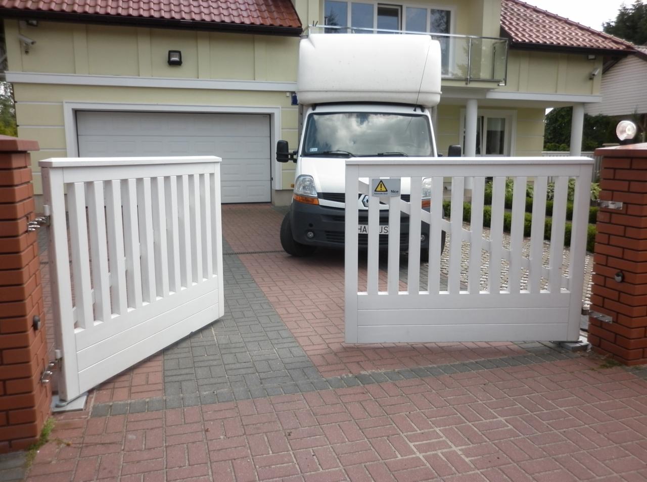 Otwarta, biała, nowoczesna brama posesyjna z pionowymi szczebelkami, na tle domu z garażem i zaparkowanego samochodu dostawczego.