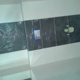 Wykończona łazienka z ułożonymi białymi i czarnymi płytkami z motywem spirali, widoczne elementy instalacji sanitarnej i naklejka producenta na jednej z płytek.