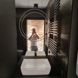 P.H.U. Filip Dutkiewicz - Nowoczesna łazienka z czarnymi ścianami, białą umywalką nablatową i okrągłą lampą wiszącą, w lustrze odbija się ceglana ściana i osoba robiąca zdjęcie.