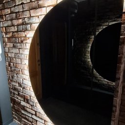 P.H.U. Filip Dutkiewicz - Ściana z cegieł z półokrągłym otworem na drzwi, podświetlona od dołu, szara podłoga z płytek.