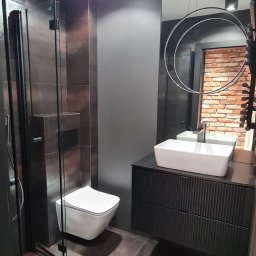 P.H.U. Filip Dutkiewicz - Nowoczesna łazienka z kabiną prysznicową, podwieszaną toaletą, umywalką nablatową na czarnej szafce z frezowanymi frontami, okrągłym lustrem i płytkami imitującymi rdzę na ścianach i podłodze.