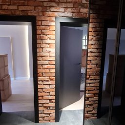 P.H.U. Filip Dutkiewicz - Wnętrze po remoncie: ściana z cegły klinkierowej, dwie czarne ościeżnice z szarymi drzwiami, szara podłoga z płytek, czarne reflektory na suficie.