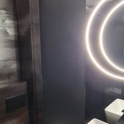 P.H.U. Filip Dutkiewicz - Nowoczesna łazienka w odcieniach szarości i czerni z podświetlanym lustrem, wiszącą toaletą i prostokątną umywalką nablatową.