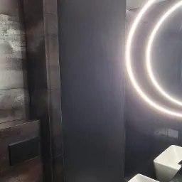 Nowoczesna łazienka w odcieniach szarości i czerni z podświetlanym lustrem, wiszącą toaletą i prostokątną umywalką nablatową.