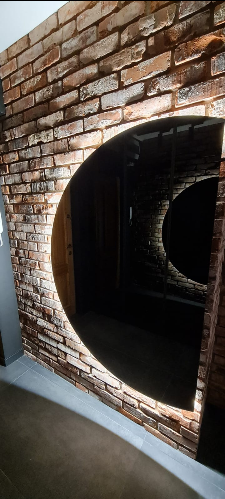 Ściana z cegieł z półokrągłym otworem na drzwi, podświetlona od dołu, szara podłoga z płytek.