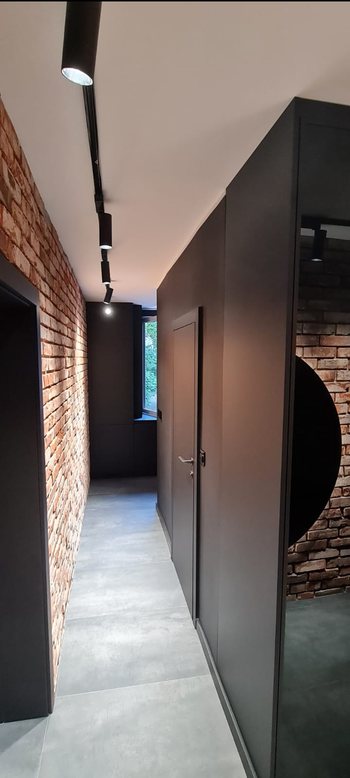 Nowoczesny korytarz z ceglaną ścianą, szarą zabudową meblową i punktowym oświetleniem na szynie.