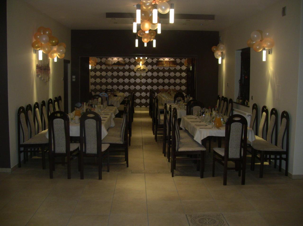 Elegancka sala bankietowa z dekoracjami: balony, oświetlenie punktowe, stoły z białymi obrusami i krzesłami. Ustawienie na uroczystość, widok w głąb sali.